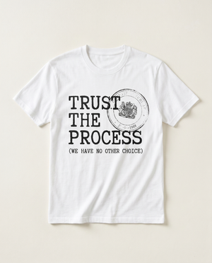 Trust The Process rubber-stamp satire tee, flat-lay on bone background
